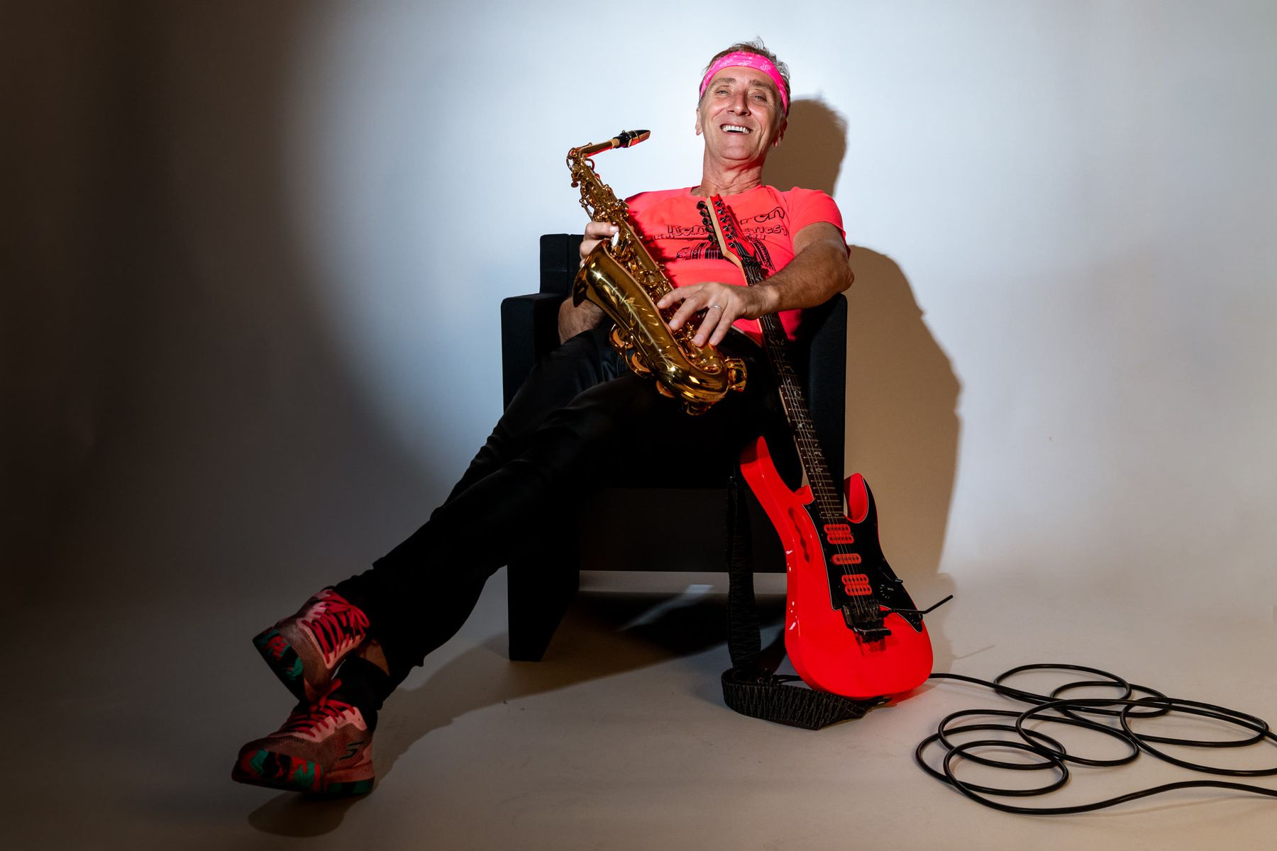 Ronnyron lachend in een fauteuil met saxofoon en gitaar